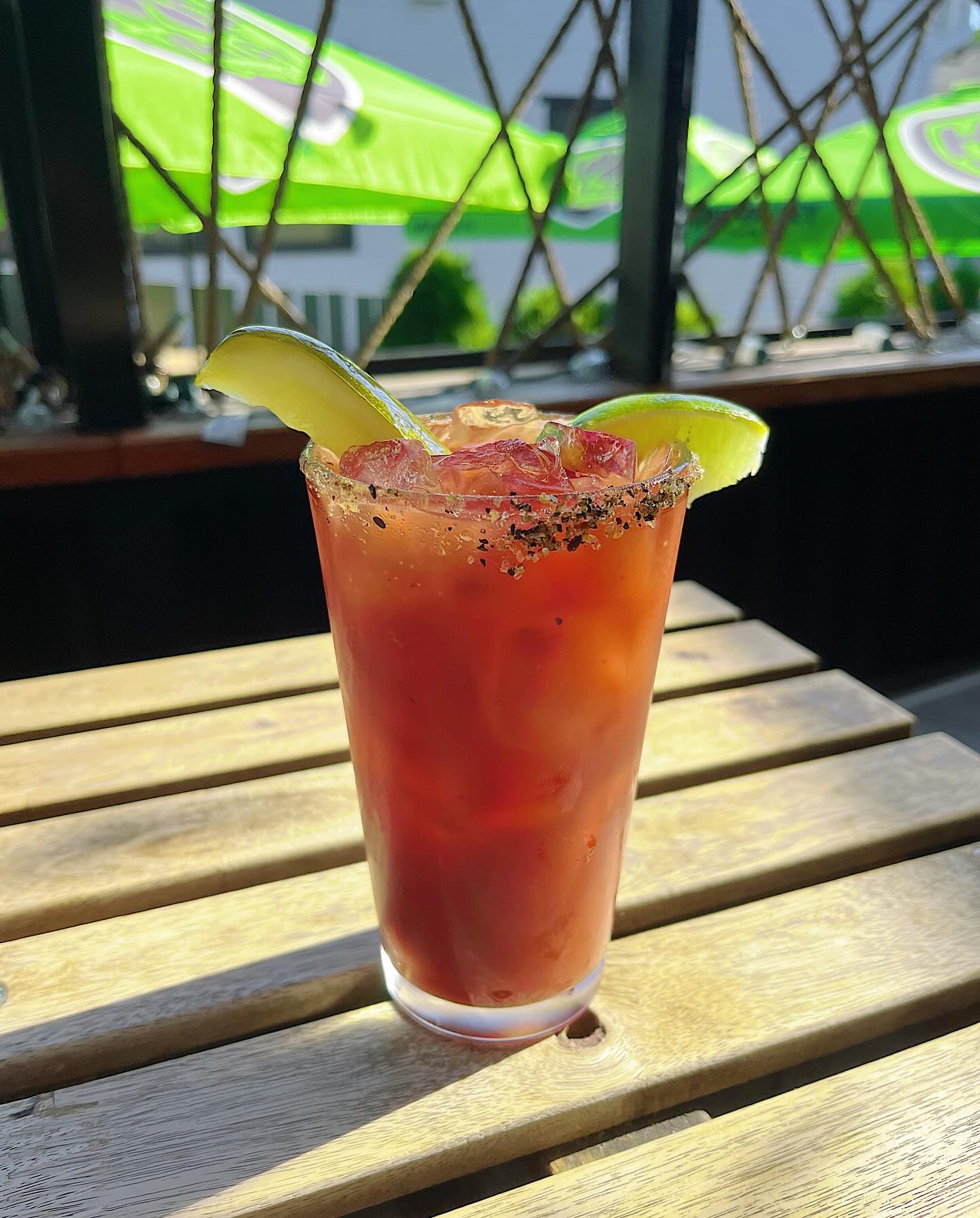 A rimmed caesar with lime wedges on the patio, green umbrellas behind