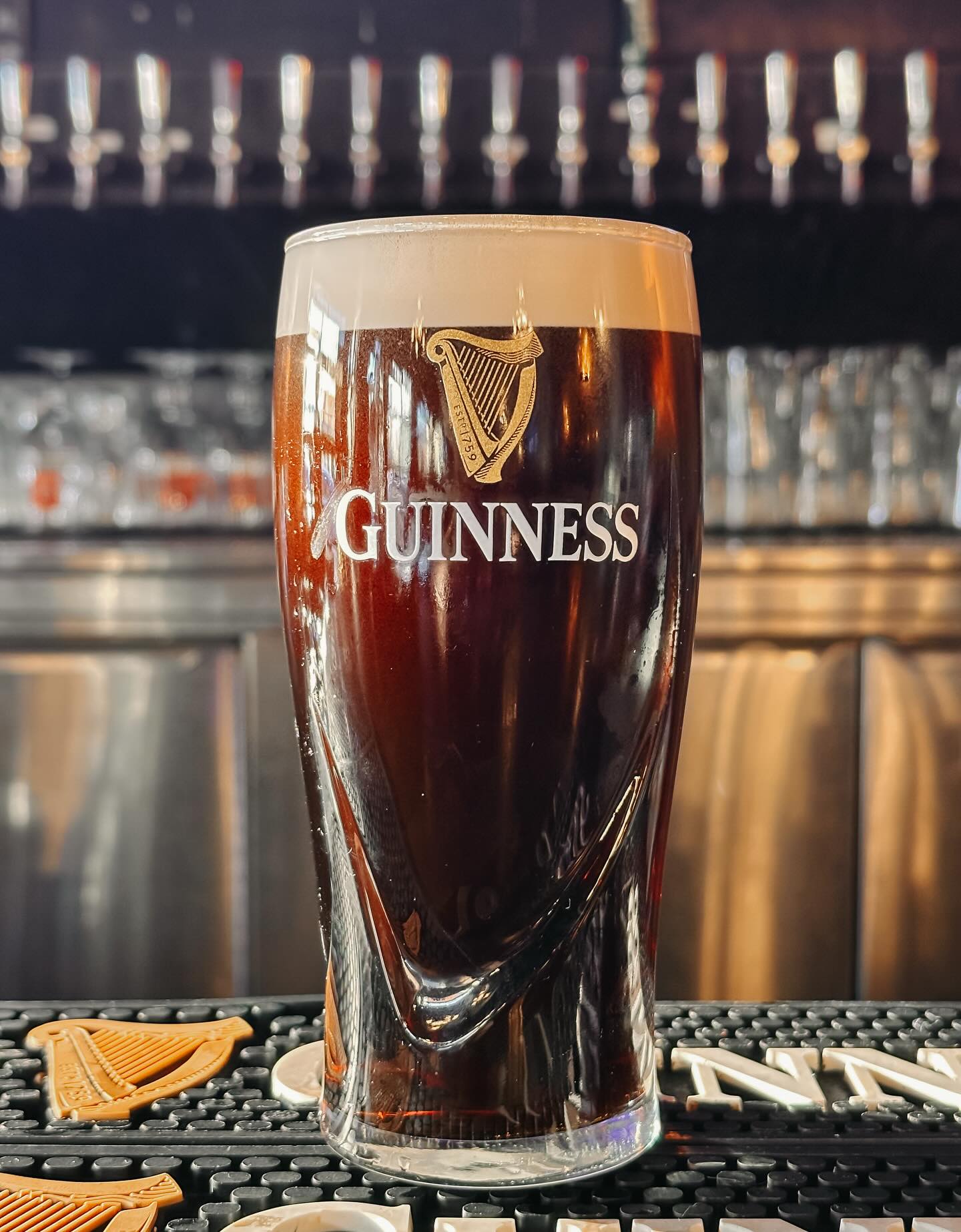 A settled pint of Guinness on the bar mat under the tap wall