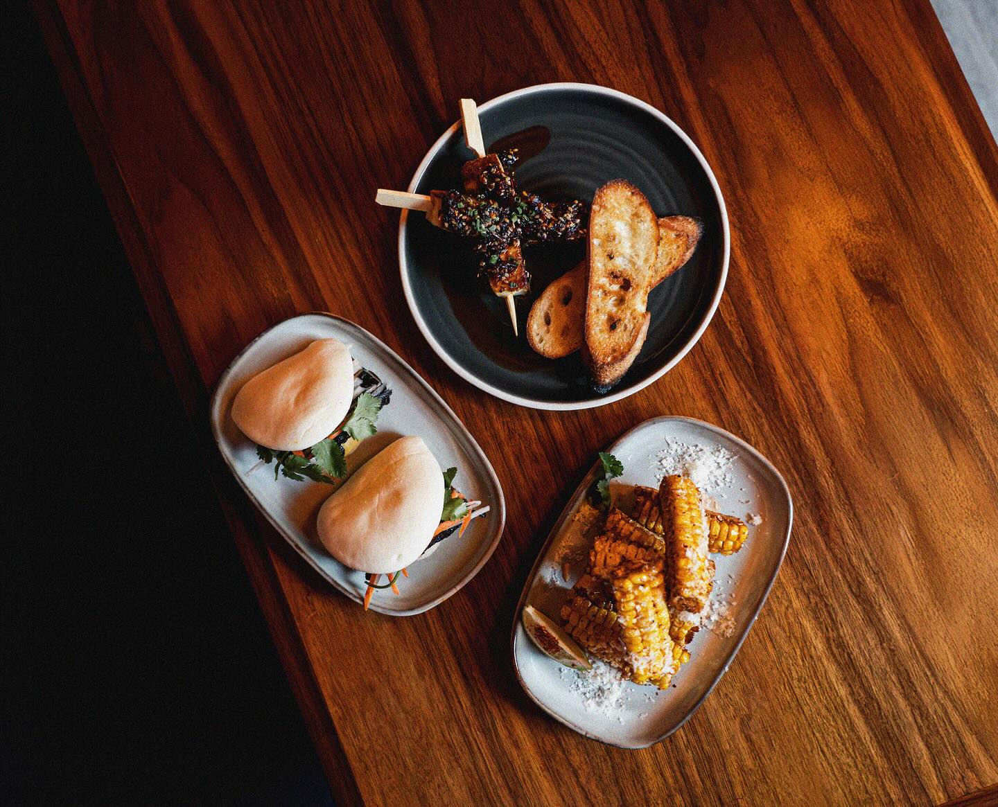 Bao buns, glazed skewers with grilled baguette, and corn ribs with cotija, shot from above