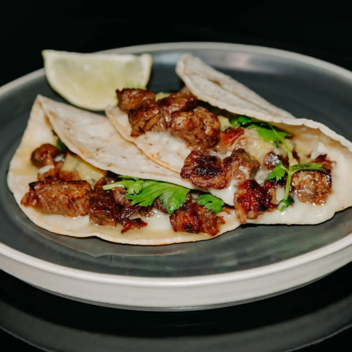 Steak tacos with melted cheese, cilantro and a wedge of lime