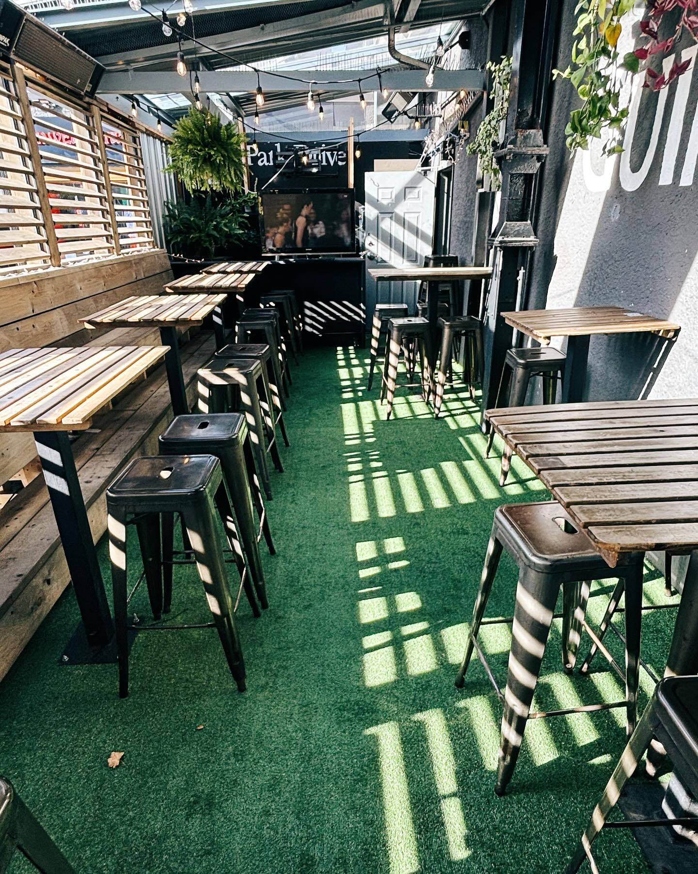The covered back patio, with high tables, stools and string lights over green turf