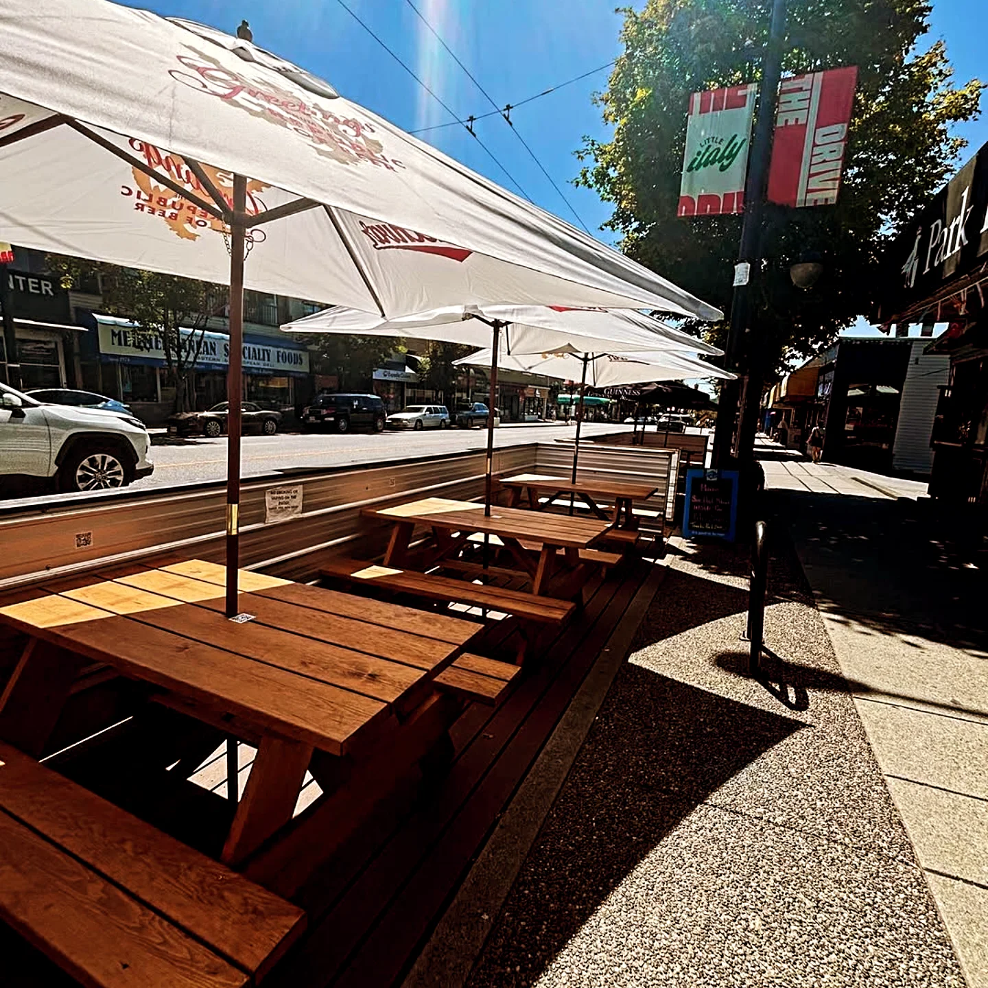 The street-side patio on Commercial Drive, picnic tables under white umbrellas in full sun
